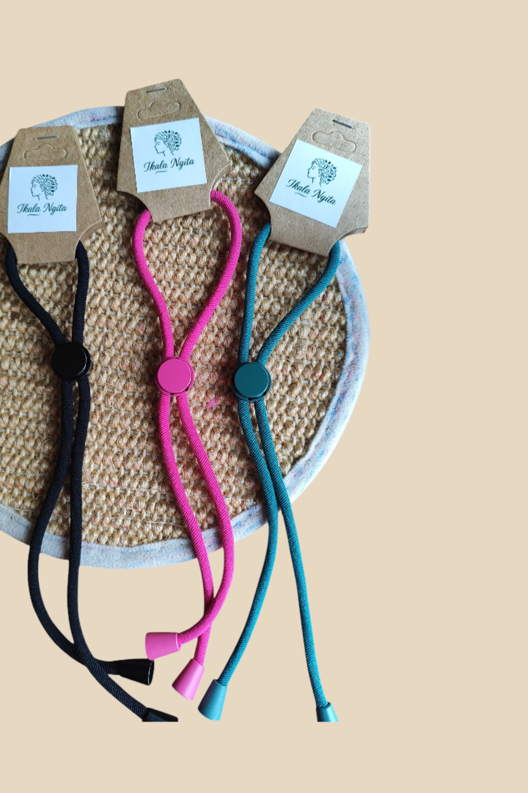 Élastiques réglables Ikala Ngita – Trois couleurs : vert, rose et noir, présentés sur support en jute