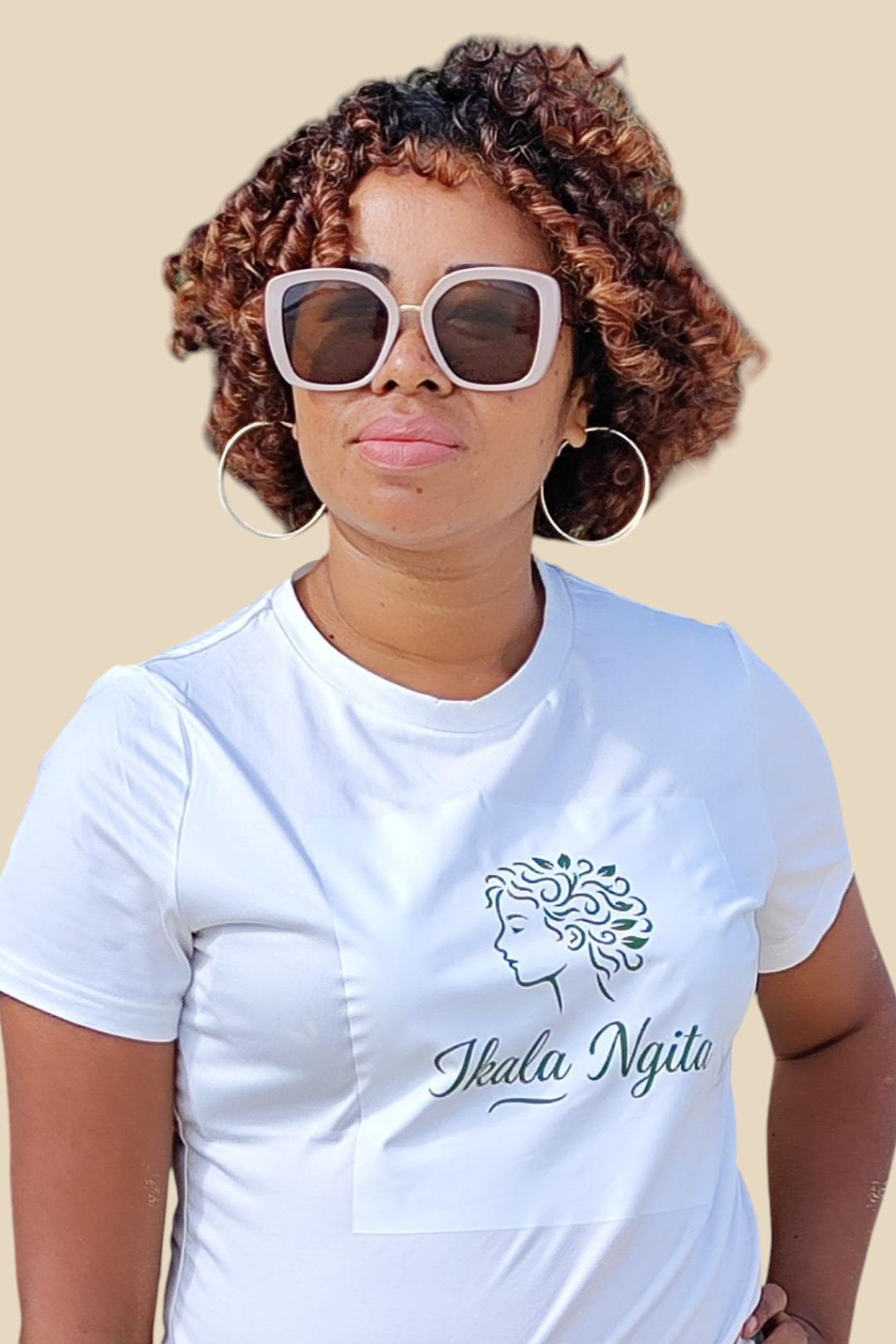 Femme aux cheveux bouclés cuivrés portant un t-shirt blanc avec le logo Ikala Ngita, marque de soins capillaires naturels pour cheveux texturés. Look estival avec grandes lunettes de soleil, incarnant l’élégance et l’identité afro-malgache