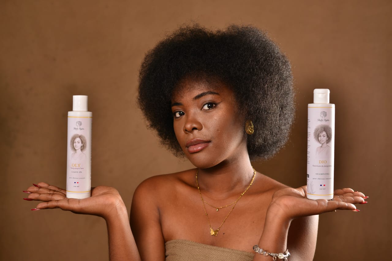 Femme aux cheveux afro présentant deux soins capillaires Ikala Ngita, illustrant une routine pensée pour les cheveux crépus et texturés.