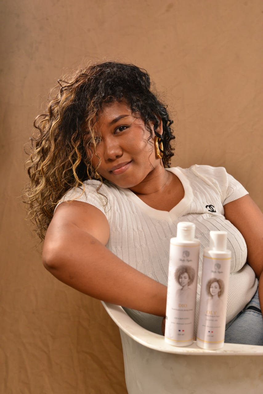 Femme aux cheveux bouclés tenant les soins capillaires Ikala Ngita, mettant en avant une routine adaptée aux cheveux texturés et à la définition des boucles.