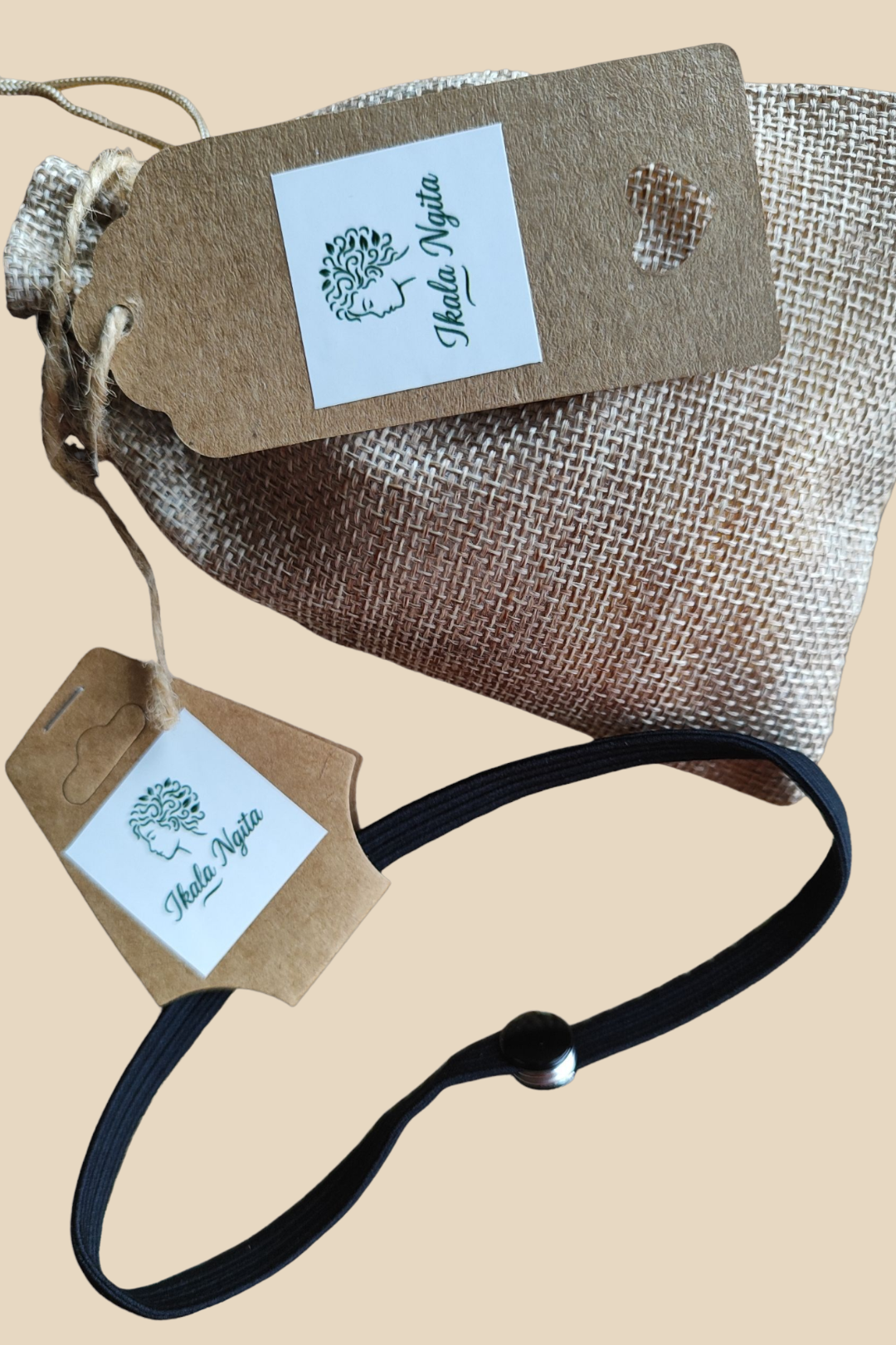 Élastique noir réglable Ikala Ngita avec bouton coulissant, présenté avec un pochon en toile de jute