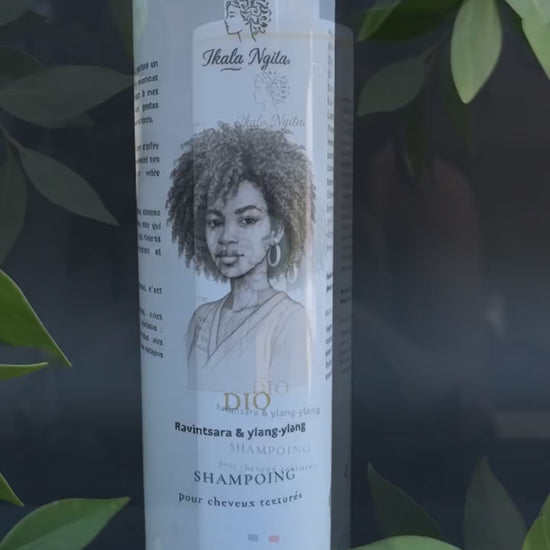 Shampoing Dio Ikala Ngita pour cheveux texturés, présenté dans l'eau au milieu de feuilles vertes en mouvement