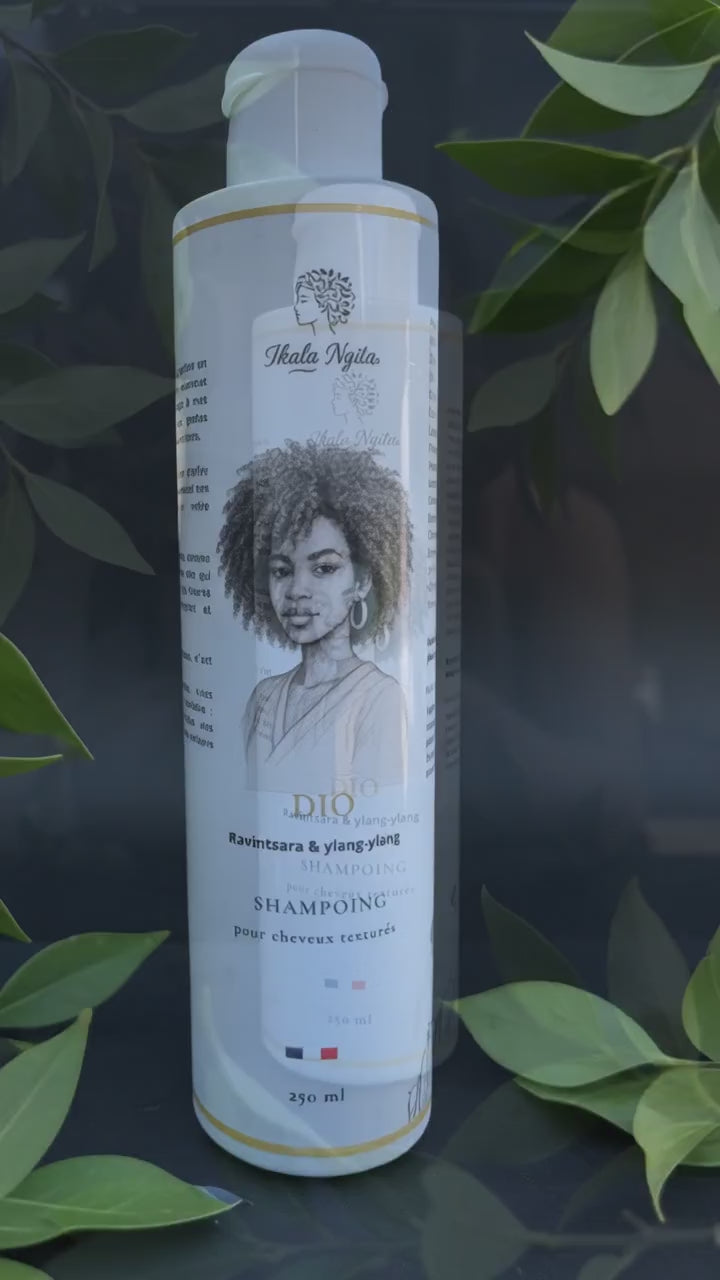 Shampoing Dio Ikala Ngita pour cheveux texturés, présenté dans l'eau au milieu de feuilles vertes en mouvement